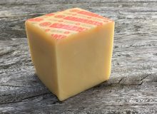 A picture of a block of Emmentaler AOP Cheese. It is positioned on a rustic wooden table