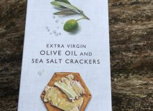 A picture of a box of the Fine Cheese Company's Extra Virgin Olive Oil and Sea Salt Crackers. There are lying on a rustic wooden table