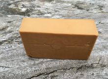 A picture showing a piece of Gjetost cheese. This brown Norwegian cheese is sat on a rustic wooden table