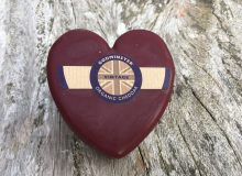 A picture showing a Godminster Heart Cheddar Cheese. It looks amazing in its burgundy wax. It is positioned on a rustic, wooden table