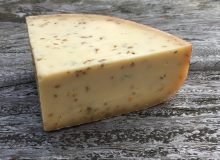 A picture of a wedge of Gouda with Cumin. It is sat on a rustic, wooden table