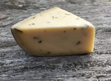 A picture of a wedge of Gouda with Truffles. It is shown on a rustic wooden table