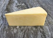 A picture showing a wedge of Gould's Extra Tasty Cheddar Cheese.It has been placed on a rustic, wooden table