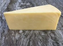 A picture of a wedge of Gould's Farmhouse Cheddar. It is positioned on a rustic, wooden table