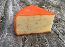 A wedge of Harlech Cheese. It is striking in its bright orange wax and pictured on a rustic wooden table.
