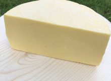 A picture of half a wheel of Heckfield Cheese. Is it positioned on a wooden board which is sat on a lawn
