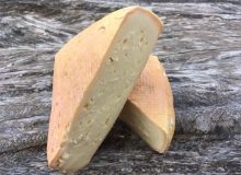 A picture showing a Highmoor Cheese that has been cut into 2 triangles. They are positioned on a rustic, wooden table