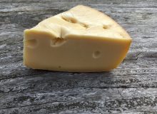 A picture of a cut wedge of the famous Jarlsberg cheese. It is sat on a rustic looking wooden table.