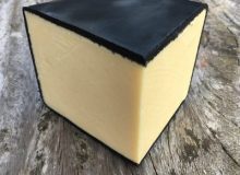 A photo of a wedge of Just Jane Cheddar Cheese. It has been placed on a rustic wooden table