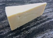 A picture of a wedge of Keen's Extra Mature cheddar. The cheese is positioned on a wooden table.