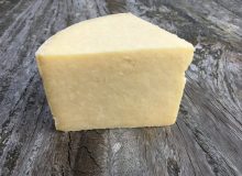 A picture showing a wedge of Kirkham's Lancashire Cheese. It is positioned on a rustic, wooden table