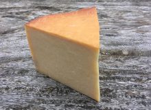 A picture of a wedge of Kirkham's Smoked Lancashire. It has been placed on a rustic wooden table.