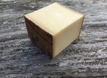 The picture shows a wedge of Le Gruyère Cheese on a wooden table