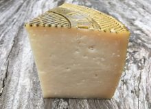 A picture showing a wedge of Manchego PDO cheese. It is positioned on a rustic, wooden table