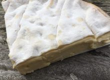 A picture of a wedge of Vacherin Mont D'Or cheese. It has been positioned on a rustic wooden table