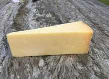 A picture showing a wedge of Montgomery Cheddar Cheese sitting on a wooden table
