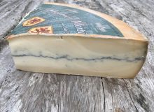 A picture of a wedge of Morbier PDO Cheese. It has been positioned on a rustic, wooden table.