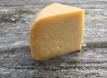 A picture showing a wedge of Old Winchester Cheese. It is sat on a rustic wooden table.