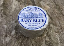 A picture depicting an Oxford Baby Blue Cheese. It is positioned on a wooden table