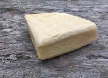 A photo of a wedge of Oxford Isis cheese. It has been placed on a rustic looking wooden table