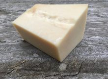 A picture showing a wedge of Parmigiano Reggiano PDO cheese. It has been placed on a rustic wooden table.