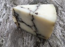 A picture of a wedge of Pecorino Moliterno Cheese. It has been placed on a rustic wooden table