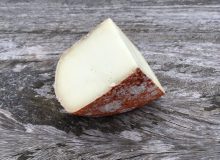 A picture showing a wedge of Pecorino Rosso cheese. It has been placed on a rustic looking wooden table.