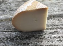 A photo showing a wedge of Rachel goat cheese. The cheese has been placed on a rustic, wooden table