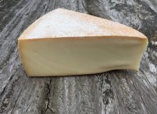 A picture of a wedge of Raclette cheese. It is positioned on a wooden table