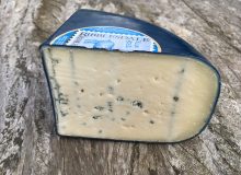 A photo of a wedge of Ribblesdale Blue Goat Cheese. It is pictured standing on a rustic, wooden table.