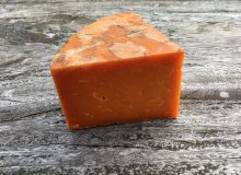 A photograph depicting Rutland Red Cheese. It has been positioned on a rustic looking wooden table