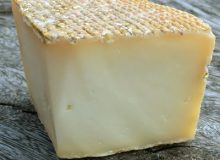 A picture of a wedge of Sheep Rustler cheese. It is stood on a rustic wooden table.