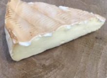 A photo of a wedge of Smoked Brie Cheese. It has been placed on a wooden table