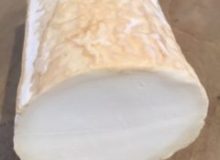 A picture of a piece of Smoked Chèvre Bûche. It has been positioned on a wooden board