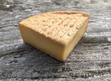 A picture of a wedge of Smoked Gubbeen Cheese. It is positioned on a rustic wooden table.
