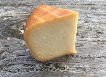 A photo of a wedge of Smoked Winchester Cheese. It has been positioned on a rustic wooden table