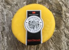A picture of a Snowdonia Beechwood Cheese. It is still in its yellow wax casing and is sat on a rustic wooden table