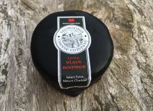 A picture of a whole little Snowdonia Black Bomber Cheese. It is positioned on a rustic wooden table