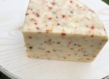 A picture of a wedge of Spitfire Cheese. You can see the flakes of chilli in the paste if the cheese. It is sat on a round board