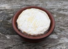 A picture of a St Marcellin PGI cheese. It is in a ceramic dish that has been placed on a rustic wooden table.