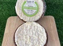 A picture showing two St Felicien cheeses. They have been placed on a wooden board with a green background