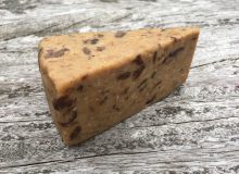 A picture of a wedge of Sticky Toffee Cheddar. It is sat on a rustic, wooden table