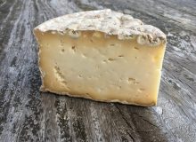 A picture showing a wedge of Stoney Cross cheese. It is positioned on a rustic wooden table.