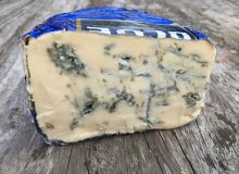 A picture of a wedge Strathdon Blue cheese. It is positioned on a wooden table