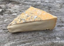 A photo of a wedge of Taleggio PDO cheese sitting on a wooden table