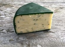 A picture of a wedge of Tintern Cheese. It looks magnificent in its green wax and is positioned on a rustic, wooden table