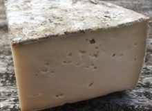 A picture showing a wedge of tomme de savoie PDO cheese. It is placed on a wooden table