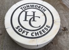 A picture of a boxed Tunworth Cheese. It has been placed on a wooden table.