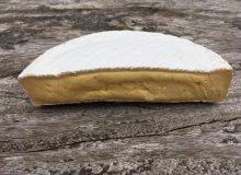 A picture of half a wheel of Waterloo Cheese. It has been positioned on a rustic, wooden table.