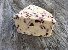 A picture of a wedge of Wensleydale with Cranberries Cheese. It is positioned on a rustic, wooden table